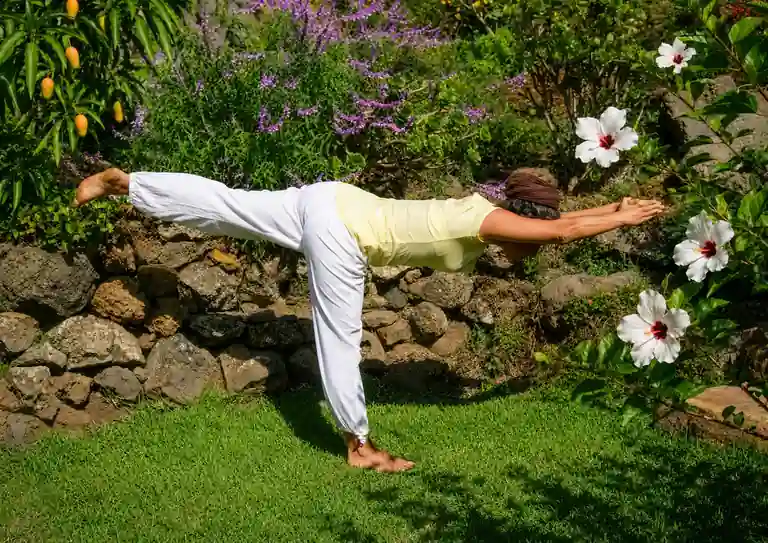 Yoga La Palma: profesora de yoga realizando una asana de equilibrio en el prado de yoga, rodeado de hibiscos en flor, en La Palma.