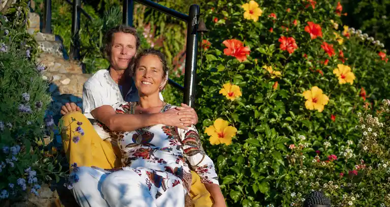 Yamuna und Olay sitzen gemütlich auf der Treppe von Vidyamor, umgeben von der üppigen Natur und den leuchtenden Blüten eines Hibiskus. Ein persönlicher Einblick in die Menschen und die Vision hinter der besonderen Retreat-Oase auf La Palma.